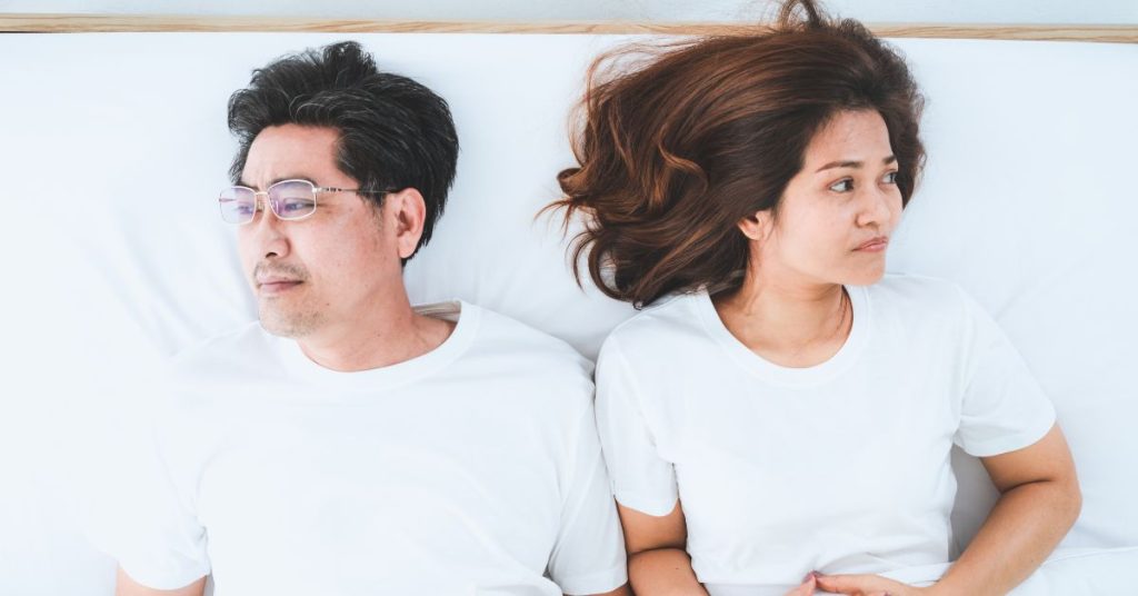 Couple laying in bed looking in opposite directions and looking unhappy