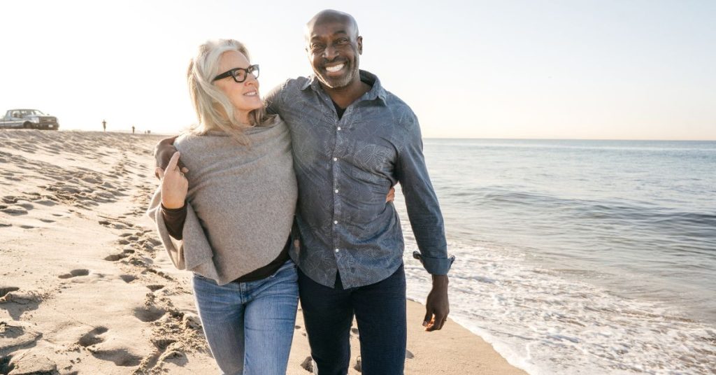 Couple over 50 walking on beach and smiling