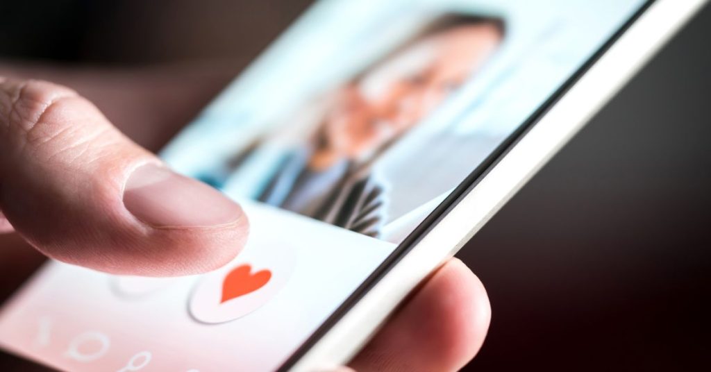 Phone with dating app up and thumb about to press heart