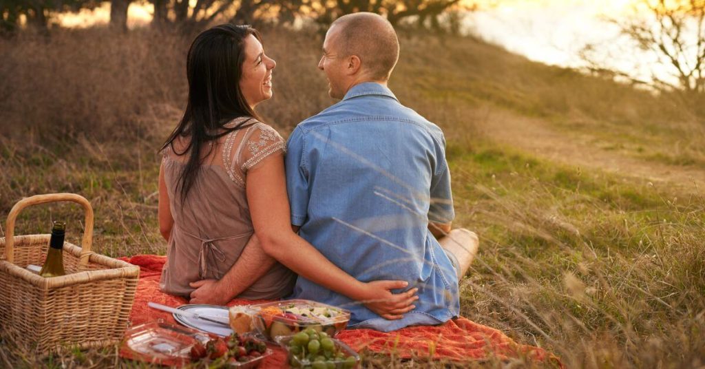 Questions to ask on your second date | Couple having a picnic on the grass sitting and laughing as they face each other