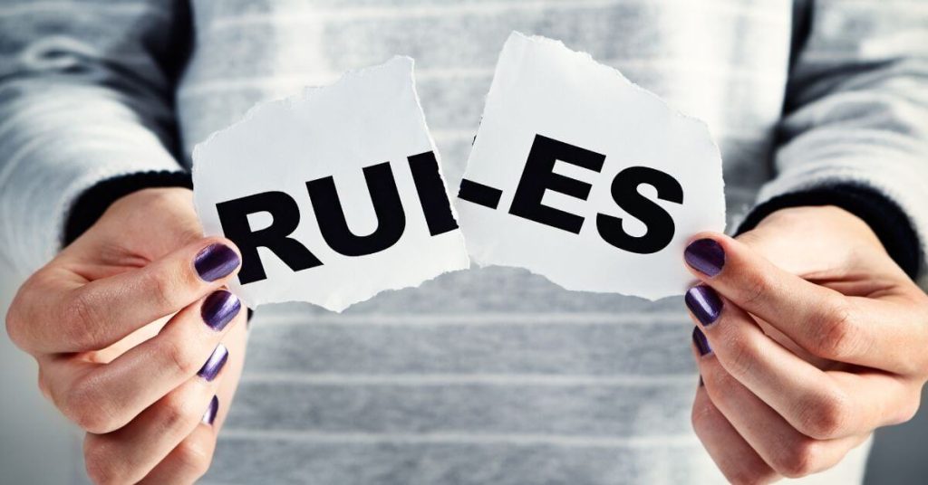 The word "rules" written on paper and being ripped by hands